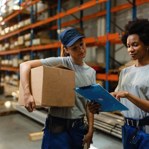 Female warehouse workers going through shipment list before the delivery. African American worker and her coworker reading order list before the shipment while working in a warehouse.